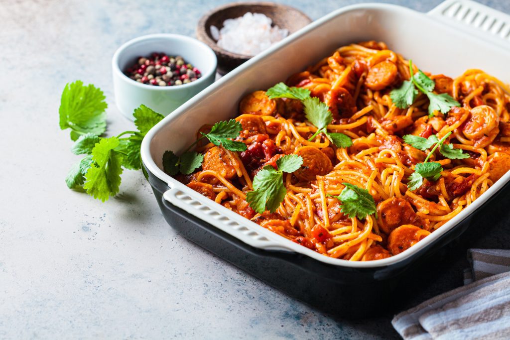 Baked spaghetti pasta with sausages in tomato sauce in oven dish.